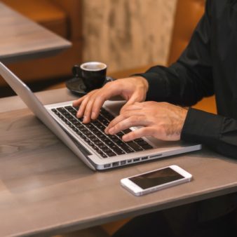 Man's hands typing on laptop in cafe